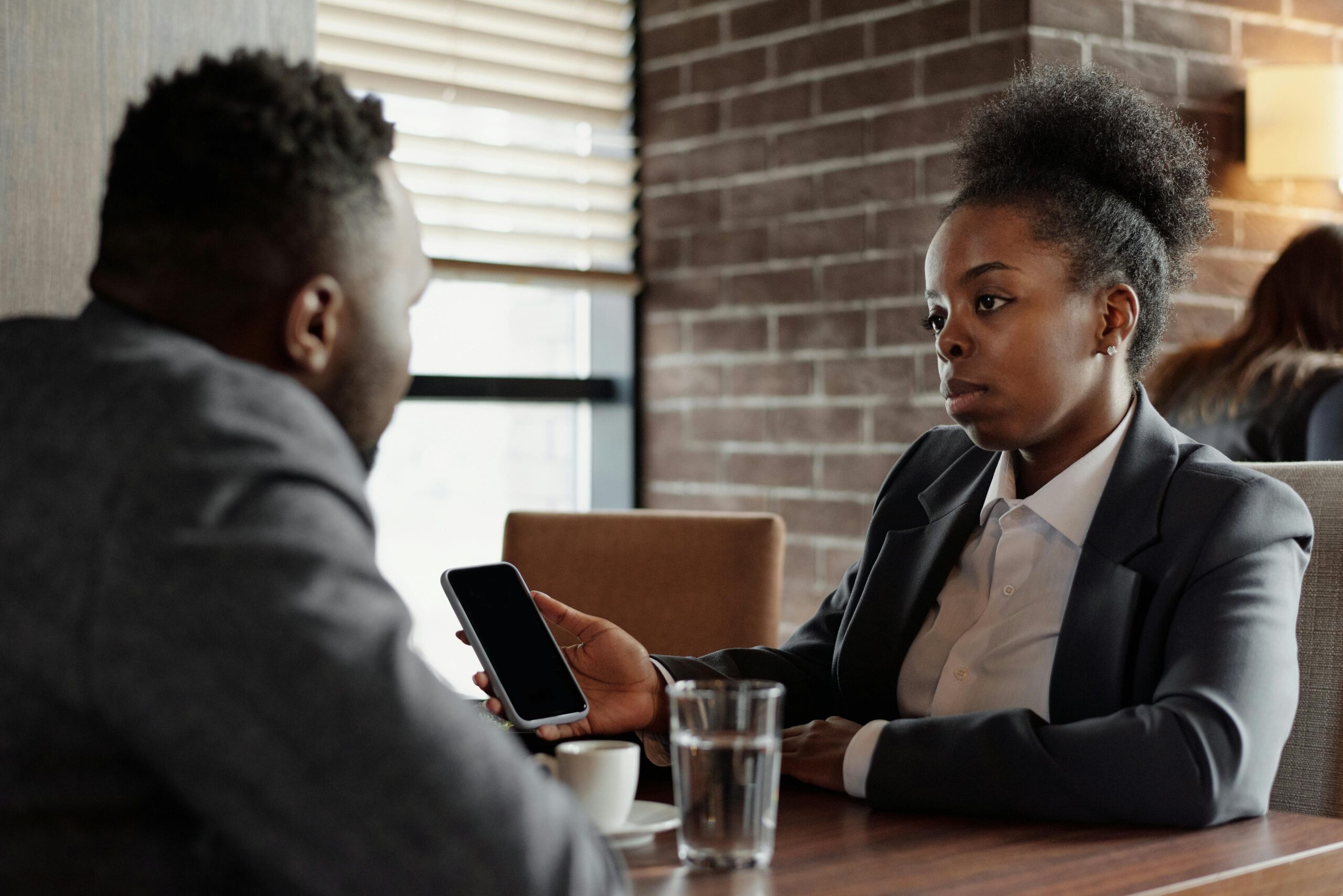 Two business professionals engage in a serious conversation while seated in a modern café.